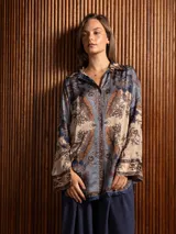 Camisa de seda de corte clásico y largo, con estampado paisley en tonos azules, marrones y beige. Presenta cuello camisero, cierre frontal con botones y mangas largas con puños rectos.