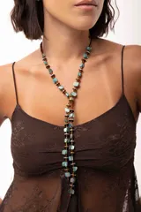 Corbatín largo estilo lariat, confeccionado con piezas de nácar teñidas en tonos turquesa y discos de piedra hematite en dorado y plateado. Cuenta con una estructura ajustable que permite regular el largo.