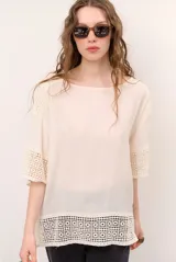 Blusa color blanco, de corte holgado y mangas tres cuartos, con detalles de encaje y bordados en las mangas y en el ruedo.