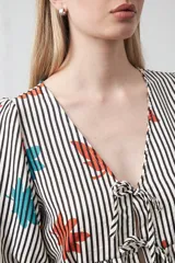 Blusa de silueta relajada con estampado de rayas verticales y motivos florales en tonos naranja y turquesa. Presenta escote en V con lazos frontales regulables, mangas cortas con leve volumen y detalle de frunce bajo el busto que aporta movimiento.