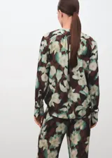 Blusa de gasa con estampado floral en tonos verdes y marrones, cuello escotado con cierre de lazo y mangas largas con puños abotonados.