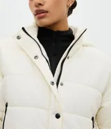 Campera puffer deportiva Get Over, color blanco con detalles de bies en color negro a lo largo de las mangas. Presenta cuello alto con capucha integrada, cierre frontal con botones a presión, bolsillos laterales con cremallera y puños con elásticos.