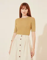 Blusa de tejido de punto metalizado en color dorado, con cuello redondo, mangas cortas y detalles de terminación en crochet en el cuello y los puños. Silueta ajustada.