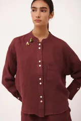 Camisa de lino color vino tinto, con cuello mao y botones blancos. Presenta un corte holgado y manga larga con puños abotonados.