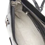 Bandolera de cuero negro con acabado brillante. Presenta dos bolsillos frontales con cierre metálico, herrajes plateados y placa metálica con logo en el centro. Incluye correa ajustable.