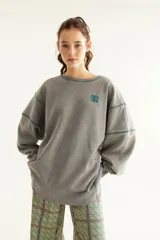 Buzo oversize gris con lavado acid wash, cuello redondo, mangas largas abullonadas y costuras decorativas en color verde. Cuenta con bordado en el pecho.