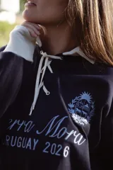 Buzo de estilo deportivo color azul marino con cuello polo y cierre frontal con cordones en color crema. Presenta puños en contraste y bordado frontal con escudo y texto.
