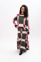 Buzo de tejido de punto con diseño geométrico de cuadros en tonos verde oscuro, rosa y crema. Presenta cuello redondo, puños y ruedo en color bordó, con mangas largas y corte holgado.