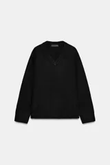 Jersey de punto negro, con cuello en V (pico) y manga larga, acabado en rib en puños, cuello y bajo.