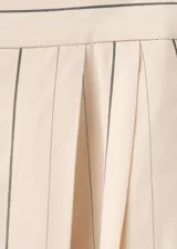 Pantalón balloon de tiro medio en color beige con estampado de rayas finas verticales oscuras. Presenta diseño abombado con bajo ajustable mediante botón.