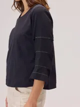 Remera de algodón color blanco, con cuello redondo y mangas tres cuartos con volados escalonados y detalles de pespuntes.