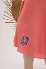 Vestido midi de lino color salmón, de corte amplio y silueta holgada. Presenta diseño con cortes irregulares y detalles de pasamanería en el escote y costuras. Cuenta con breteles dobles tipo cuerda y ruedo asimétrico.