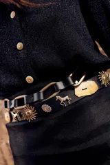 Cinto ancho de cuero marrón con apliques metálicos decorativos en forma de sol, caballo y herraduras, acompañado de tachas.