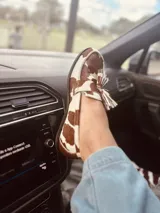 Alpargata mocasín con estampado animal print de vaca en tonos marrón y blanco, con detalle de borlas en la parte delantera.