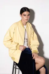 Campera estilo bomber de cuero vacuno en color amarillo pastel, con corte oversized y diseño retro. Presenta cuello, puños y pretina de tejido de algodón acanalado en tono a juego, cierre frontal y bolsillos laterales.