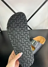 Sandalias negras con plantilla color suela y dos tiras anchas con hebilla metálica ajustable.