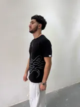 Remera de algodón color negro con estampado gráfico abstracto en tono gris en la parte inferior derecha. Presenta cuello redondo reforzado y corte regular.
