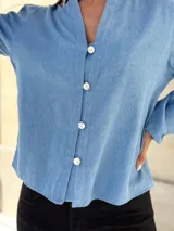 Camisa de jean celeste con cuello redondo, cierre frontal con botones y mangas largas abullonadas con puños ajustados.