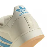 Championes Adidas Superstar edición especial Messi, color crema con las icónicas tres tiras en azul celeste. Presenta el logo de Messi grabado en el lateral y en el talón, con la clásica puntera de goma y suela de color goma.