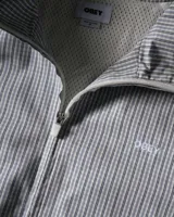 Campera tipo rompevientos de la marca Obey, con diseño a cuadros pequeños en tonos azul y blanco. Presenta cuello alto, cierre frontal completo, bolsillos laterales y detalles de líneas negras contrastantes que recorren el frente y las mangas. Incluye el logo de la marca bordado en el pecho.