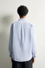 Camisa de corte regular fit confeccionada en tejido de algodón y lino, en color celeste. Presenta cuello abotonado, manga larga con puño abotonado, un bolsillo de parche en el pecho y cierre frontal con botones.