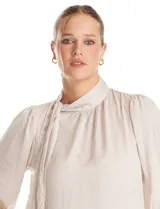 Blusa negra de acabado satinado con cuello alto fruncido, detalle de lazo para anudar y cierre lateral con botones. Presenta mangas largas estilo balloon con puños ajustados.