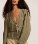 Blusa tipo bata de algodón color verde oliva, con escote en V, cierre frontal mediante lazos, mangas largas y detalles de bordados florales y encaje en el frente.