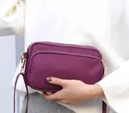 Cartera bandolera rectangular de nylon impermeable, con tres compartimentos con cierre y correa regulable.