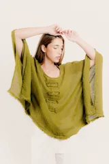 Blusa verde oliva de lino con cuello redondo y mangas anchas. Presenta detalle de tres apliques rectangulares con flecos en el frente y terminación desflecada en el ruedo.
