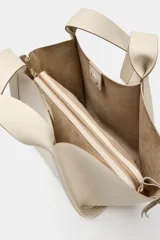 Bolso formato shopper de color beige, con detalle de pespuntes, cremalleras laterales con tiradores, doble asa y compartimento interior extraíble con cierre imantado.