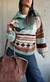 Sweater de tejido de punto con diseño a rayas horizontales y patrón geométrico en tonos verde, marrón y beige. Presenta cuello alto con cierre frontal, mangas largas abullonadas con puños ajustados y corte holgado.