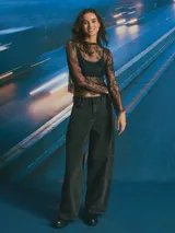 Top de encaje negro con diseño floral, manga larga y cuello redondo. Presenta un acabado festoneado en el ruedo y mangas.