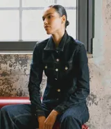 Campera femenina entallada marca Cortelle, confeccionada en denim de algodón con cuello camisero, mangas largas con puños abotonados y cierre frontal con botones metálicos. Presenta recortes estructurales que realzan la silueta y bolsillos frontales con solapa.