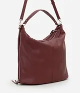 Bolso tipo hobo de gran tamaño en color bordó, confeccionado en poliuretano. Presenta una estructura desestructurada, cierre superior, correas dobles (una de mano y una larga desmontable) y cierres laterales decorativos con tiradores.