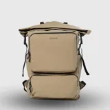 Mochila urbana de diseño funcional en color mostaza, confeccionada en material repelente al agua. Cuenta con cierre superior enrollable con hebillas ajustables, un compartimento frontal grande con cierre, un bolsillo inferior adicional con el logo de la marca, compartimentos internos organizadores, funda acolchada para laptop y bolsillos laterales para botellas.