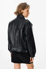 Chaqueta de cuero sintético negro con textura granulada, corte oversize, cuello camisero, cierre frontal con botones a presión, bolsillos frontales con solapa y charreteras en los hombros.