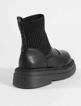 Botas tipo chunky de color negro, con caña de tejido elástico acanalado y base de goma gruesa dentada. Confeccionadas en cuero sintético.