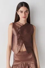 Top sin mangas de estilo cruzado, confeccionado en tela satinada color cobre. Presenta un diseño corto con cierre frontal mediante tiras finas para anudar y cuello redondo.