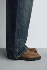 Zapato tipo Mary Jane de hombre, color marrón, fabricado en piel con acabado serraje (gamuza). Presenta cierre con hebilla lateral, detalle de bordón en el empeine y suela gruesa con volumen.