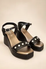 Sandalias de plataforma con cuña, confeccionadas en cuero negro con punta cuadrada y plantilla metalizada. Tienen una tira delantera decorada con tachas metálicas redondas y una tira al tobillo con hebilla regulable.
