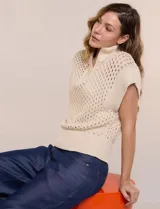 Buzo de punto color marfil, confeccionado en algodón calado con cuello alto acanalado y medio cierre metálico dorado. Presenta mangas cortas estilo japonesa con puños anchos y un zócalo acanalado en el ruedo.