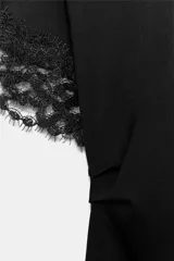 Camiseta negra de algodón con cuello redondo, manga corta y detalle de aplicación de encaje a tono en los puños. Presenta un diseño con bajo asimétrico y frunce lateral.
