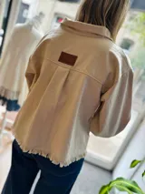 Campera color beige de gabardina con corte clásico, cierre frontal con botones y ruedo con flecos.