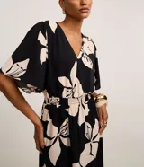 Vestido evasé midi de airflow negro con estampado de flores color crema, escote en V, sisa alargada, mangas cortas amplias y lastex en la cintura.