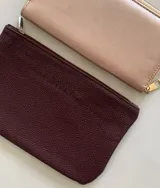Sobre billetero de cuero sintético con textura granulada en color borra de vino. Cuenta con cierre superior y bolsillo interno.