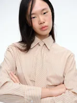 Camisa de corte clásico con estampado de rayas verticales en tonos beige y blanco. Presenta cuello camisero, cierre frontal con botones y corbata integrada del mismo tejido y estampado.