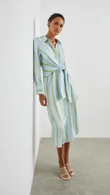 Vestido camisero midi celeste con rayas verticales blancas y amarillas, de manga larga con puños abotonados y lazo ajustable en la cintura.