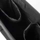 Cartera tipo tote de diseño estructurado en color negro, confeccionada en material sintético. Cuenta con doble asa superior fija, correa larga regulable y extraíble, bolsillo frontal con cierre metálico y logo circular grabado en la parte inferior.