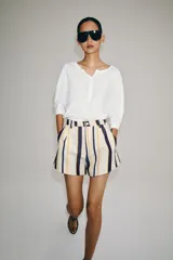 Shorts de tiro medio con trabillas en la cintura y cierre frontal con cremallera y botón. Presenta pliegues delanteros y bolsillos laterales ocultos en la costura, con un diseño de rayas verticales multicolor.