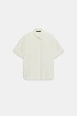 Camisa oversize de popelina con estampado de rayas verticales en tonos blanco y amarillo, cuello de solapa, manga corta con vuelta y cierre frontal de botones.